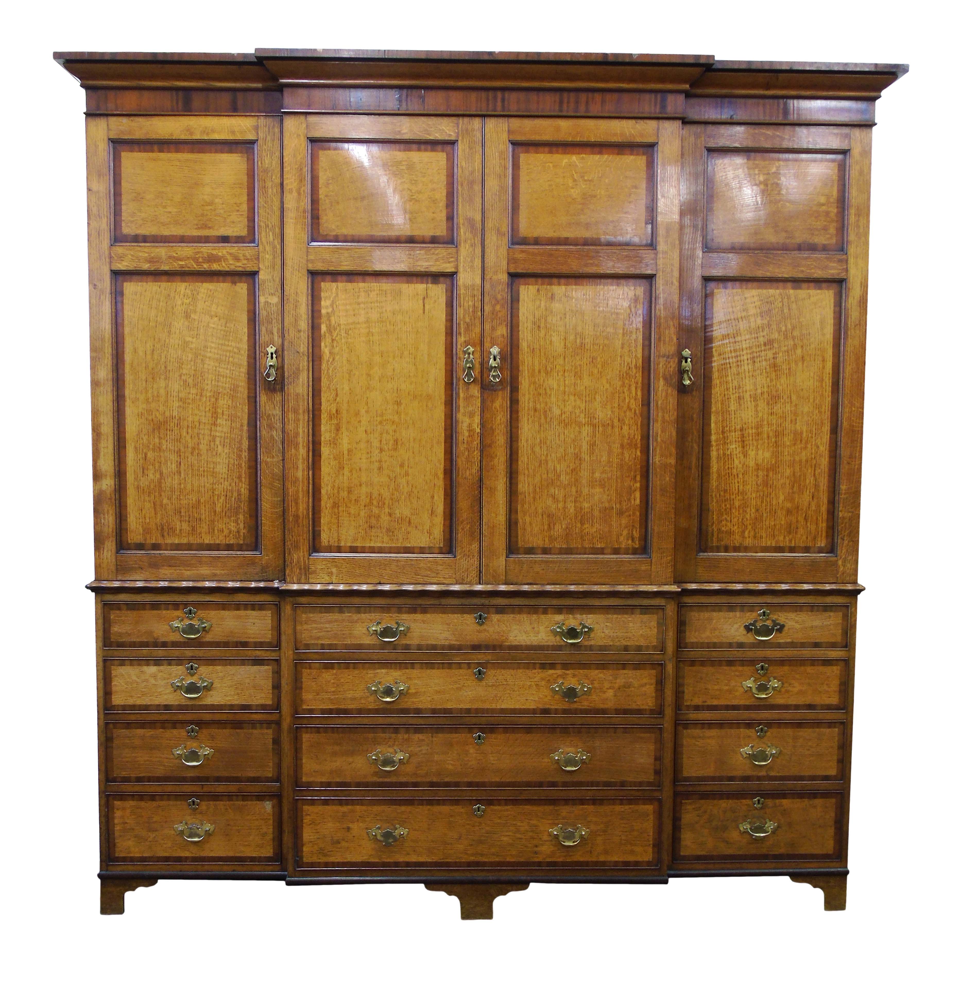 Early 19th century oak and mahogany veneered breakfront housekeepers cupboard, ogee cornice above four two panel doors, interior with fixed shelves (right hand cupboard with two short drawers), base with wavy moulding, range of four long and eight short drawers, each with brass handles, all standing on bracket feet, width 211cm (83"), depth 56cm (22"), height 231cm (91").