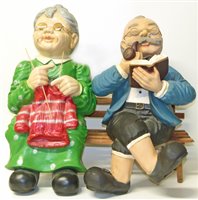Lot 98 - Painted plaster figure group of a lady and gentleman sitting on a bench knitting and smoking a pipe.