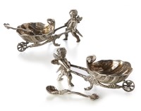 Lot 166 - A pair of German silver salts, in the form of cherubs pushing shell form wheelbarrows, complete with shell salt spoons with lamprey handles